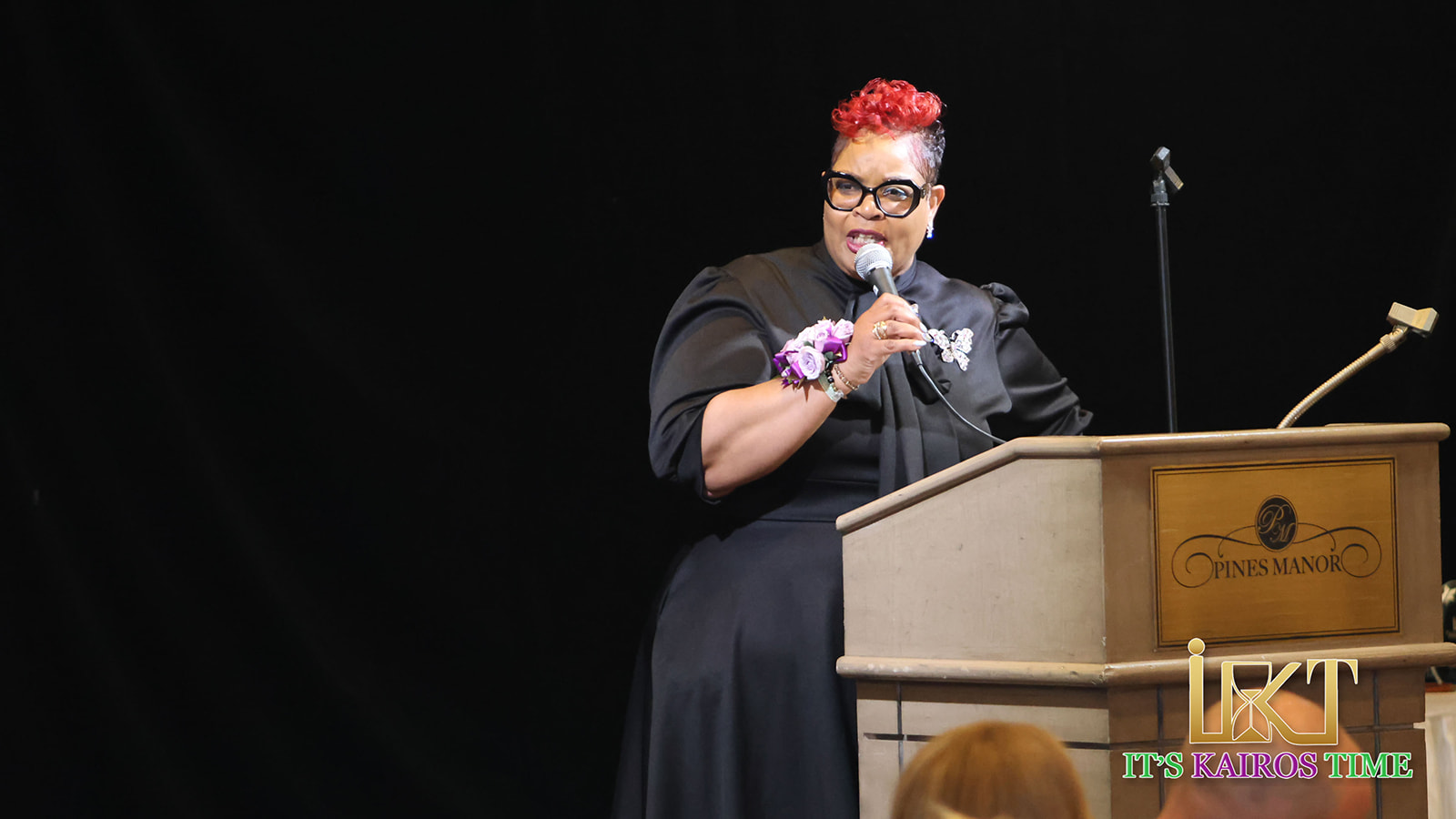 Woman with red hair and floral corsage speaking